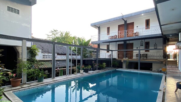 A swimming pool with a metal ladder, surrounded by potted plants and a building with a balcony. - New Wijaya Hotel (Kalasan)