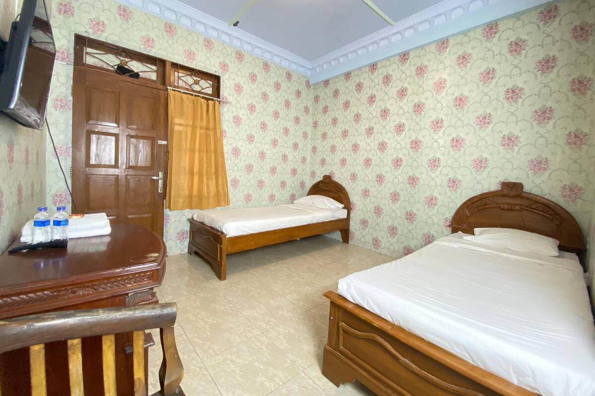 Una habitación con dos camas de madera, un escritorio de madera, una televisión y un armario.