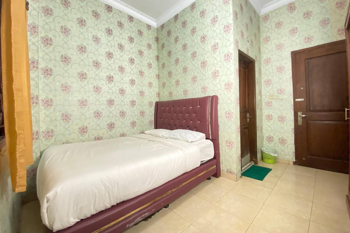 Un dormitorio con una cama, papel tapiz floral, una puerta de madera y un tapete verde.