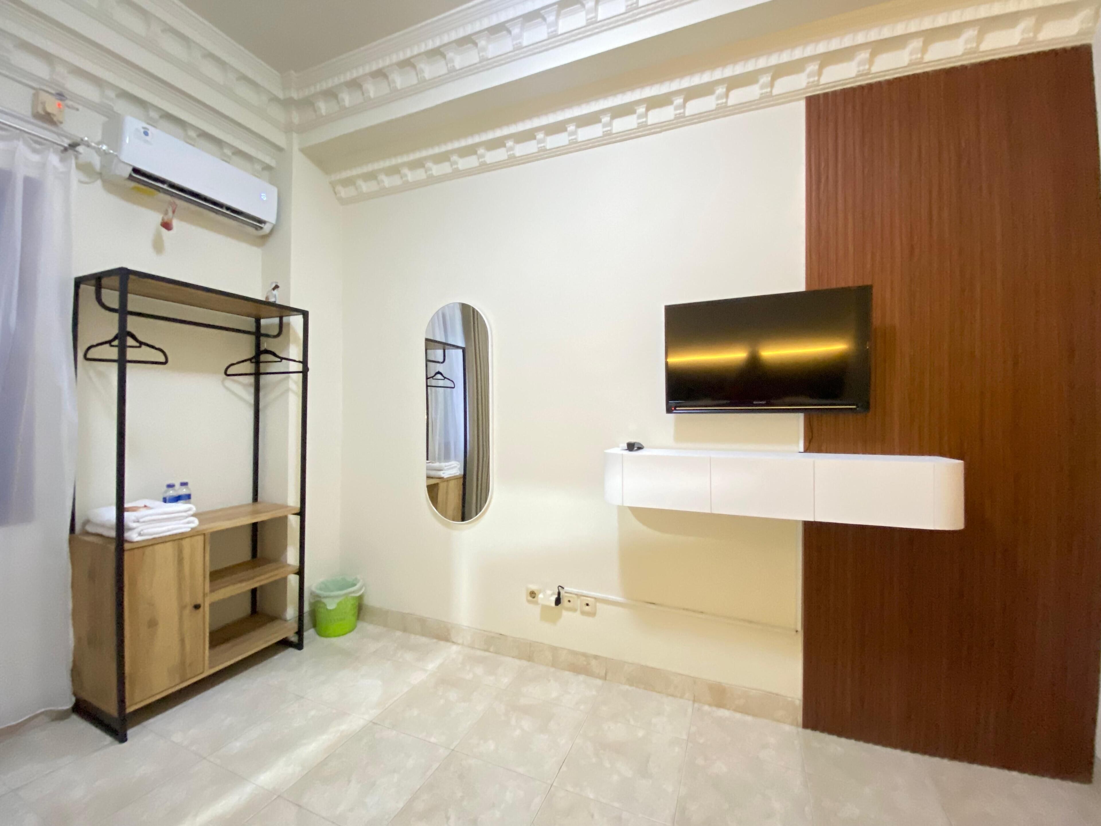A hotel room with a wooden wardrobe, a mounted TV, a mirror, and a shelf with towels.