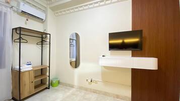 A hotel room with a wooden wardrobe, a mounted TV, a mirror, and a shelf with towels.