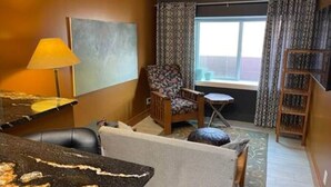 Une chambre d’hôtel avec une grande fenêtre, un canapé, un fauteuil, une petite table et une lampe.