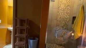 Une salle de bain avec une douche, une étagère en bois et une serviette jaune.