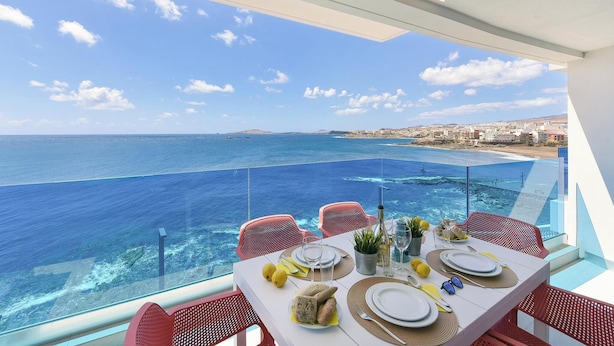 A dining table set for four with a view of the sea and a cityscape.