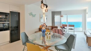 A modern kitchen with a glass dining table, a built-in oven, and a view of the sea through large windows.