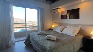 A bedroom with a large bed, two bedside lamps, a window with curtains, and a painting on the wall. - ERNESTINA VILLAGE (Villa Carlos Paz)