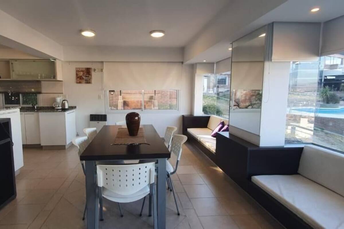 A modern living room with a dining area, a TV, and a large window offering a view of the outdoors.