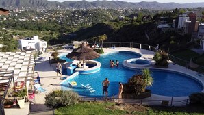 A swimming pool area with multiple pools and a thatched-roof structure. - ERNESTINA VILLAGE (Villa Carlos Paz)