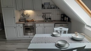 Een moderne keuken met witte kastjes, een ingebouwde oven, een spoelbak en een eethoek met een tafel gedekt voor twee personen.