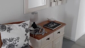 Een kamer met een houten stoel, een wit schuifkastje, een spiegel en een aantal haken aan de muur.