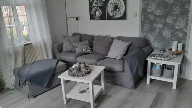 Een moderne woonkamer met een grijze bank, een salontafel en een bijzettafeltje met decoratieve objecten.
