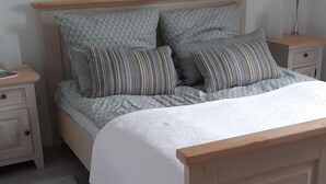 Een slaapkamer met een houten bedframe, grijze beddengoed en een grijs vloerkleed.
