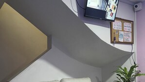 A white leather sofa with teal cushions, a mounted television, a bulletin board, and a potted plant. - A 5 minutos del aeropuerto (Bogotá)