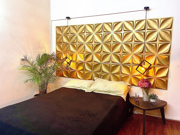 A bedroom with a bed, a nightstand, a potted plant, and a decorative wall panel. - A 5 minutos del aeropuerto (Bogotá)