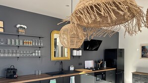 A modern kitchen with dark cabinetry, a wooden countertop, a built-in stove, and a hanging woven light fixture. - Villas Ambiance 21 Elégance Méditerranéenne à Portiragnes, Entre Terre et mer (Portiragnes)