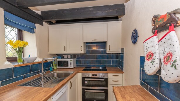 Een compacte keuken met witte kastjes, een magnetron, een dubbele oven en houten aanrechtbladen.