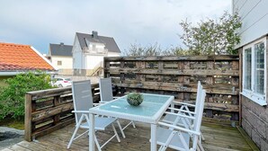 A wooden deck with a glass table and white chairs, surrounded by a wooden fence. - 4 Person Holiday Home in Kungshamn (Kungshamn)