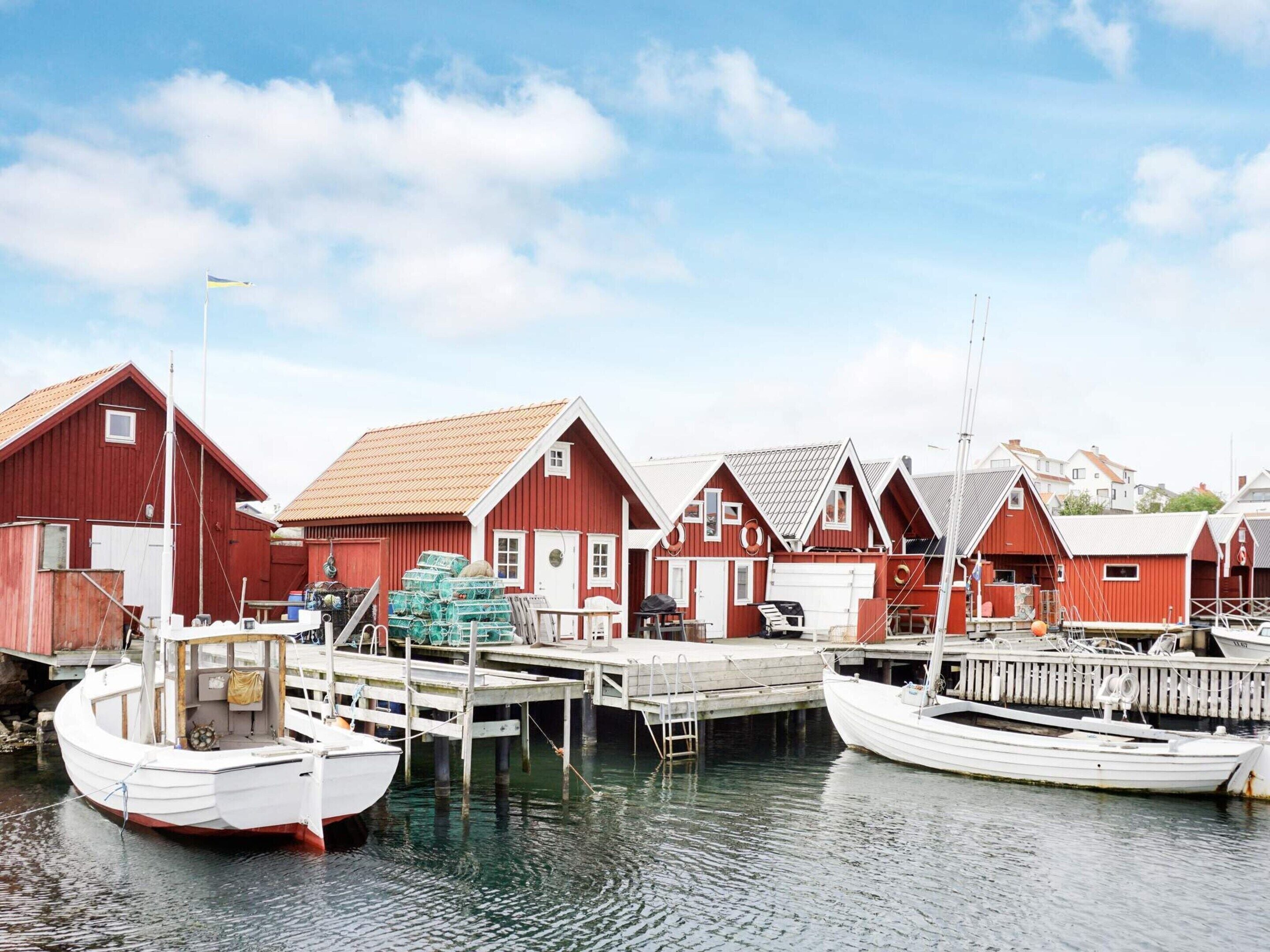 Une rangée de maisons en bois rouges, avec des quais, des bateaux et un ciel dégagé.