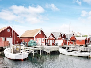A row of red wooden houses with docks, boats, and a clear sky.