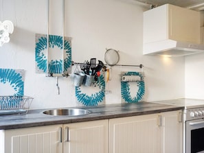 A kitchen with a sink, cabinets, and a stove. There are kitchen utensils hanging on a rack.