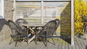 A wooden deck with a table and four wicker chairs, a wooden fence with flags, and a bicycle to the right. - 4 Person Holiday Home in Kungshamn (Kungshamn)
