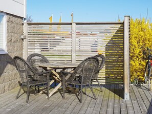 A wooden deck with a table and four wicker chairs, a wooden fence with flags, and a bicycle to the right. - 4 Person Holiday Home in Kungshamn (Kungshamn)