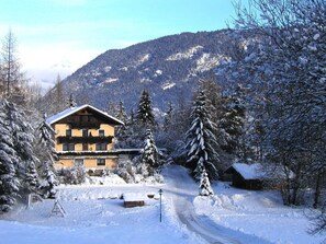 A snow-covered lodge with a wooden exterior, surrounded by snow-laden trees and a mountain backdrop. - Holiday Home Chalet Astrid (Sautens)