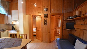 L’intérieur chaleureux d’un chalet comprend une table à manger en bois, un canapé, un téléviseur et un coin cuisine.