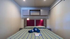 A hotel room with a bed, two nightstands, a red headboard, and a wall-mounted shelf above the bed. - Rivaverde Family Camping Village Lodge Deluxe für 5 Personen (Marina di Ravenna)