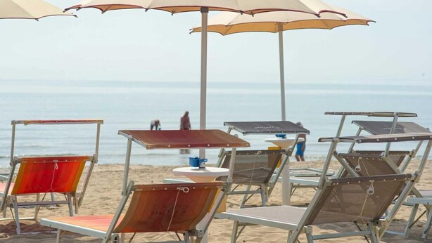 Beach chairs and umbrellas arranged on the sand, with a view of the ocean in the background. - Rivaverde Family Camping Village Lodge Superior für 3 Personen (Marina di Ravenna)