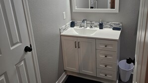 A bathroom with a white vanity, a mirror, a sink, and a trash can. - Cute and Cozy! (Van Buren)