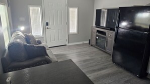 A compact living space with a sofa, a dining table, a kitchen area including a refrigerator and oven, and a ceiling fan. - Cute and Cozy! (Van Buren)