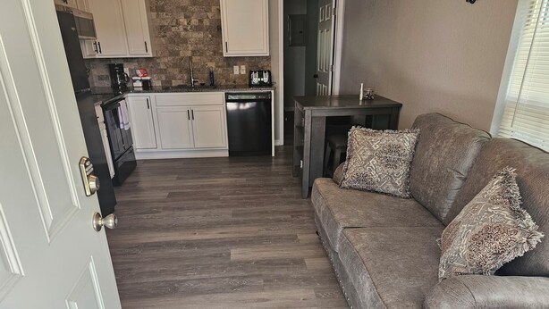 A modern kitchen with white cabinets, a stone backsplash, and a dark wood floor. - Cute and Cozy! (Van Buren)