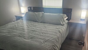 A bedroom with a bed, two bedside tables with lamps, a window with blinds, and a door. - Cute and Cozy! (Van Buren)