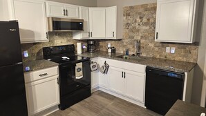 A kitchen with white cabinets, a black refrigerator, a stainless steel microwave, a black stove, a coffee maker, and a dishwasher. - Cute and Cozy! (Van Buren)