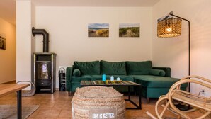 A cozy living room with a green sofa, a woven ottoman, a wicker rocking chair, a small table, and a wall-mounted lamp. - Baltic Sea Mermaid, Green Lagoon (Ostseebad Wustrow)