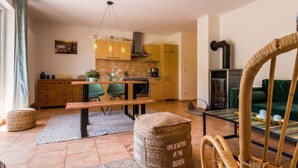 A modern kitchen with wooden cabinets, a dining table, and a bench. There is a sofa and a wicker chair in the living area. - Baltic Sea Mermaid, Green Lagoon (Ostseebad Wustrow)