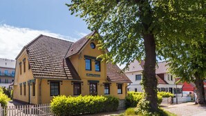 A yellow building with a tiled roof, a wooden fence, and green bushes. - Baltic Sea Mermaid, Green Lagoon (Ostseebad Wustrow)