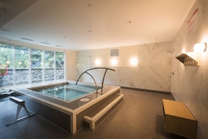A spa area with a hot tub, seating, and a view of greenery outside.
