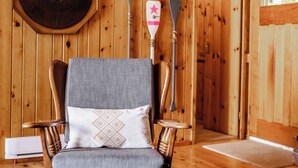 Ein Holzhütten-Interieur mit einem Holzstuhl, einem an der Wand befestigten Paddel und einer Tür, die nach draußen führt.