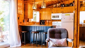 Eine gemütliche Küchenzeile im Blockhausstil mit Holzwänden, einer Bar mit Sitzgelegenheit und einem bequemen Sessel.
