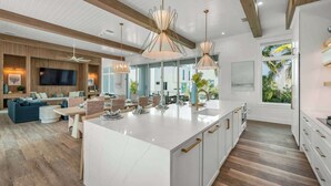 Une cuisine moderne dotée d’un grand îlot central, de poutres en bois et de grandes fenêtres offrant une vue sur la verdure.