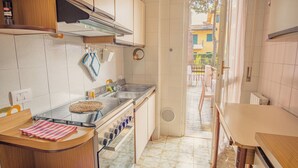 Een kleine keuken met een fornuis, spoelbak en uitzicht op een balkon.