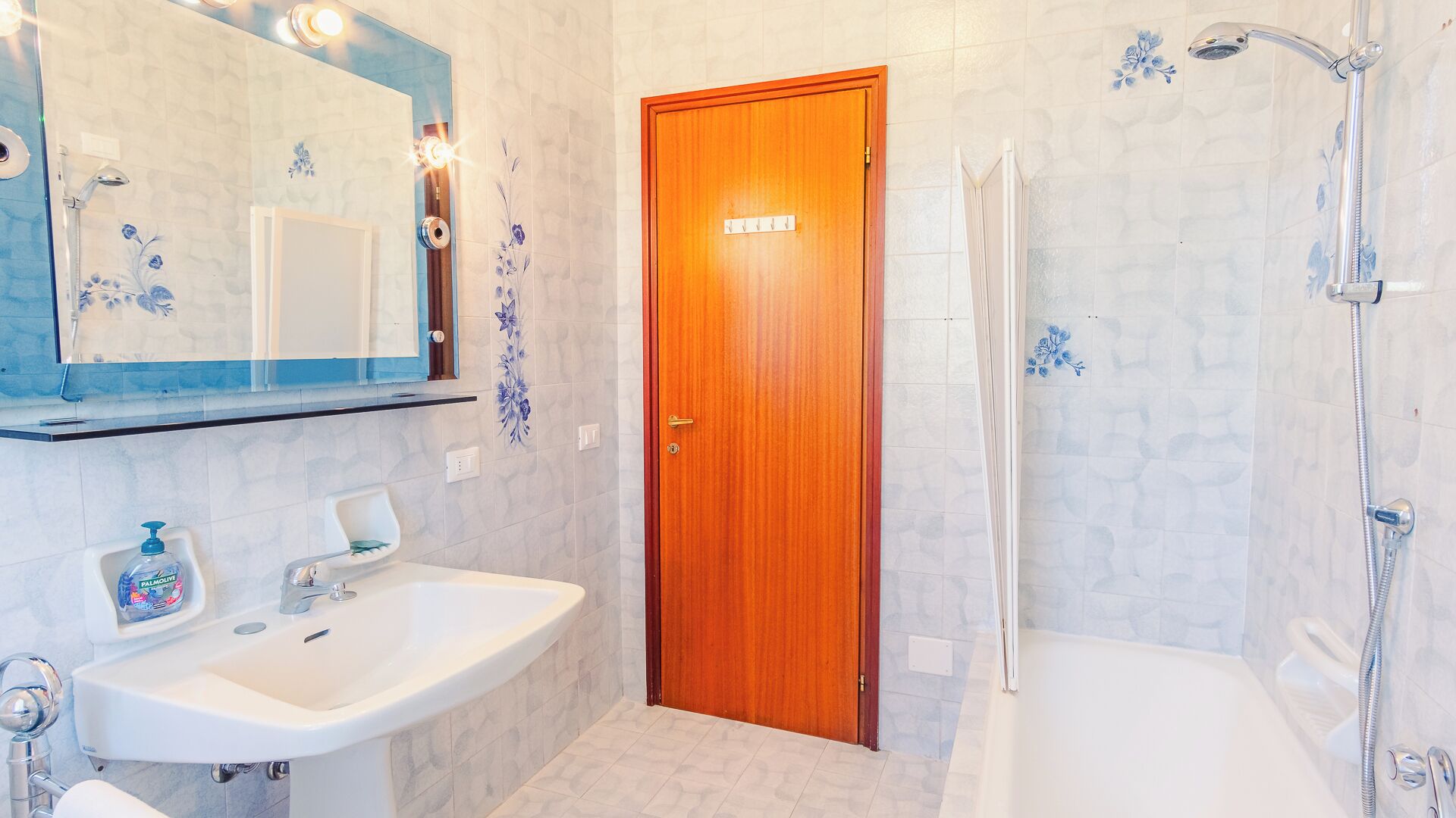 A bathroom with a wooden door, a white sink, a mirror, and a shower area.