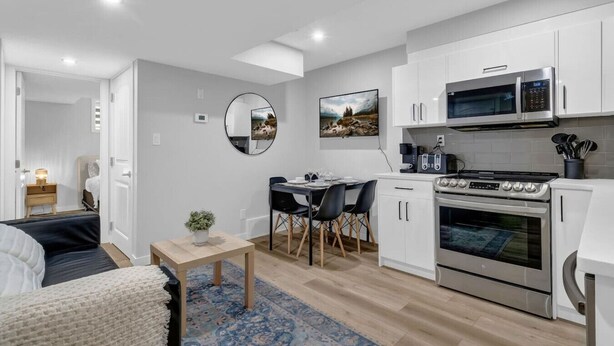 A modern kitchen with white cabinets, a microwave, a stove, and a dining area with a table and chairs. - ModernSuite*NearAirport*2 Queens*ROKU (Edmonton)