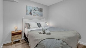 A bedroom with a white bed, a bedside table with a lamp, and wall art above the bed. - ModernSuite*NearAirport*2 Queens*ROKU (Edmonton)