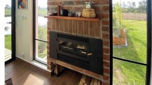 A modern living room with a brick fireplace, a large window, and a view of a garden. - House with mountain views

 (Checa)