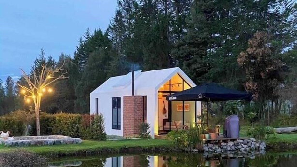 A modern house with a glass door entrance, a small outdoor seating area, and a pond in front. - House with mountain views

 (Checa)
