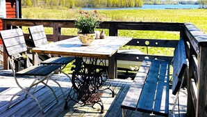 Eine Holzterrasse mit Tisch, Stühlen, einer Kübelpflanze und Blick auf einen See.