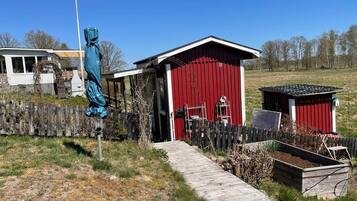 A red wooden shed with a door, a small attached structure, a wooden fence, and a wooden pathway leading to the shed.